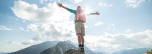 Young Adult stands proud atop a mountain celebrating success and overcoming obstacles in substance use disorder recovery